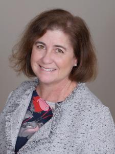 A women with brown hair wearing a gray suit smiling at the camera